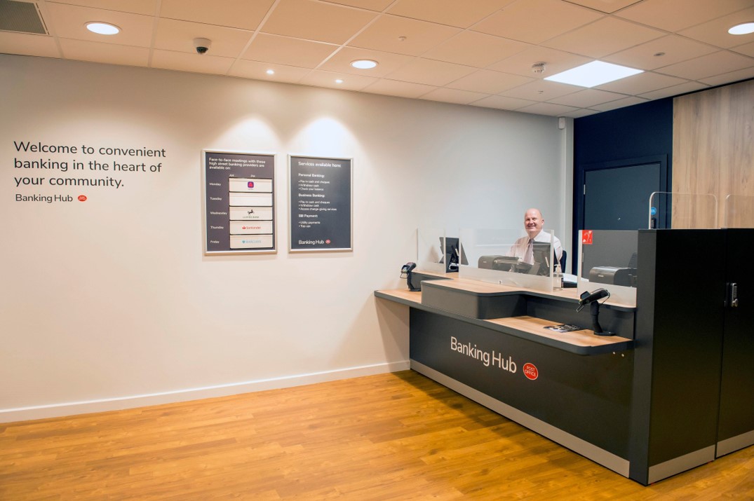 Inside a banking hub looking at the main counter with a member of Post Office staff smiling behind it.